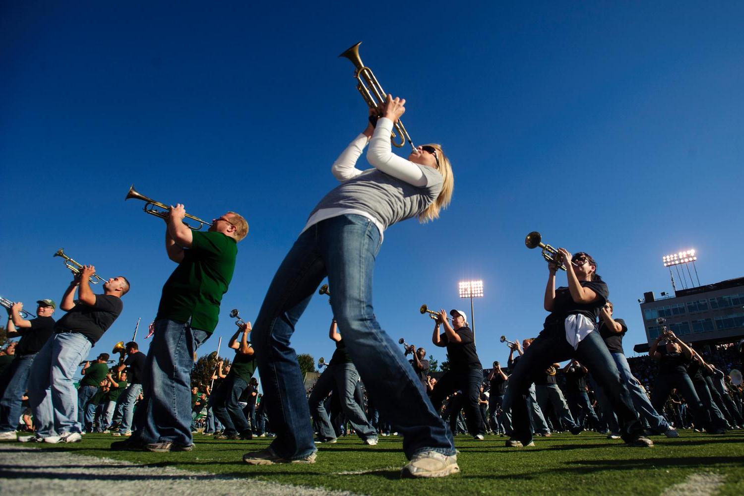 Marching 110 alumni play their horns on the field